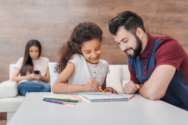 istock smiling father drawing with  african american daughter while mother using smartphone behind 814962446