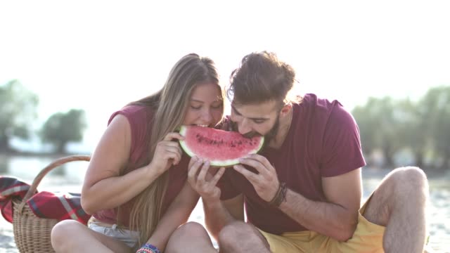 Young couple sharing watermelon at the beach