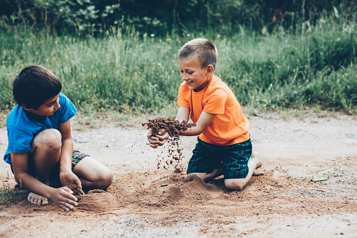 Two boys playing with soil outdoors.