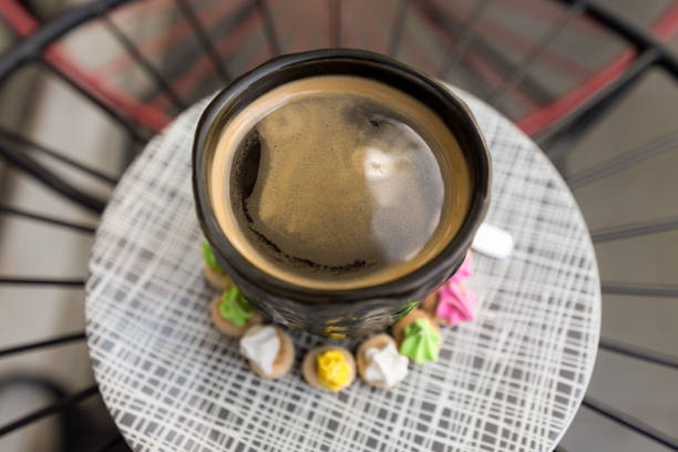Hot Americano coffee with crema top in a classy black glass surrounded buy colourful classic Ice Gem sweets biscuits on a patterned plate.