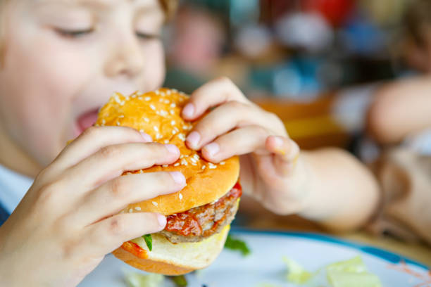istock Cute healthy preschool boy eats hamburger sitting in school canteen 814992906