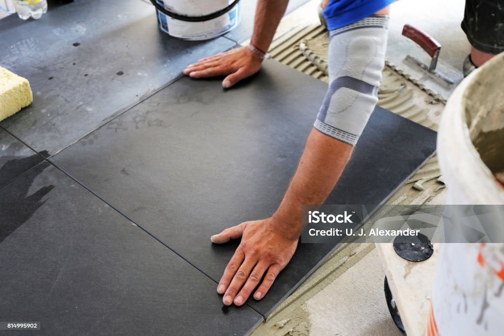 Worker laying floor tiles Worker laying floor tiles, close up Tiled Floor Stock Photo