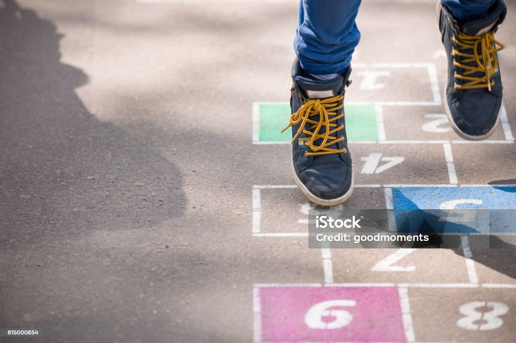 Closeup de pernas do garoto e amarelinha desenhada no asfalto. Criança brincando de amarelinha no playground ao ar livre em um dia ensolarado. actividades ao ar livre para crianças. - Foto de stock de Pátio de escola royalty-free