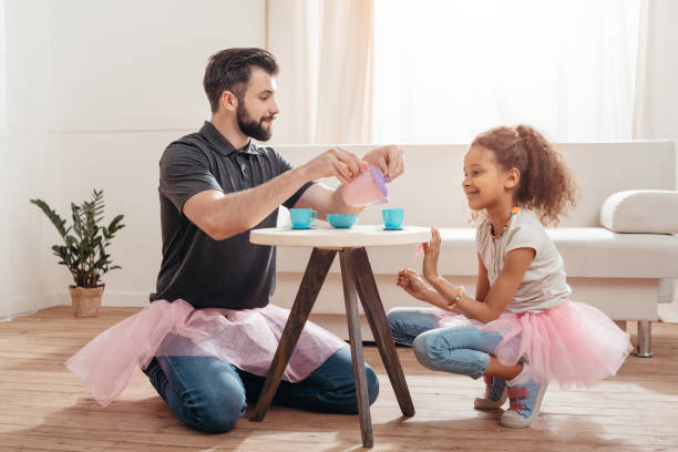 multicultural father and little daughter having tea party at home