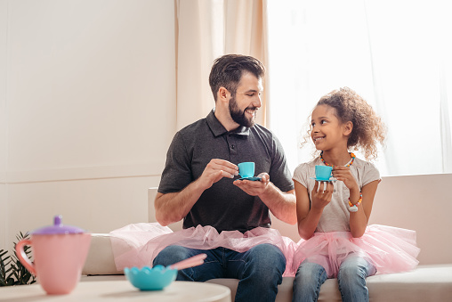 multicultural father and smiling daughter having tea party at home