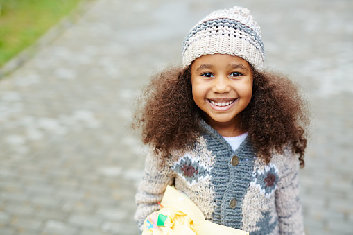 Portrait of cute African-American girl looking up at camera and smiling wearing knit hat and sweater on warm autumn day