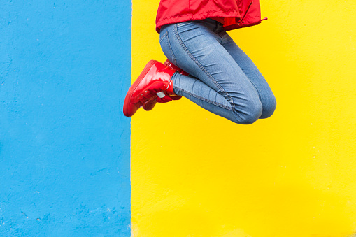 Woman in red sneakers jumping against yellow and blue wall