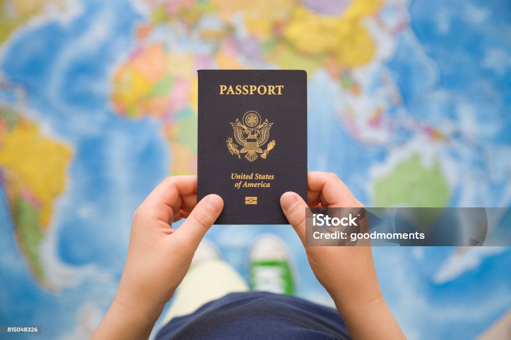 Child's hand holding US passport. Map background. Ready for traveling. Open world. Passport Stock Photo