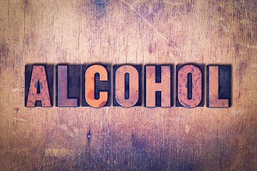 The word Alcohol concept and theme written in vintage wooden letterpress type on a grunge background.
