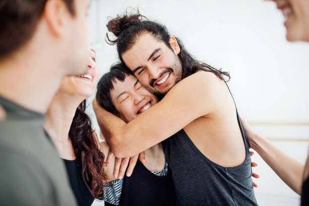 Man embracing woman amidst friends. Young dancers are standing at ballet studio. They are in sportswear.