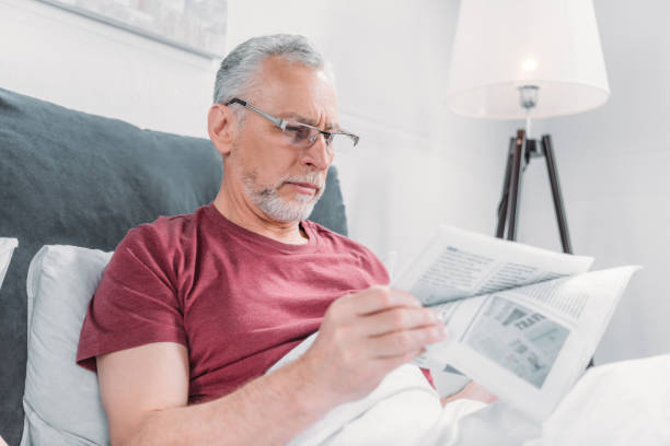 istock focused senior man reading newspaper while lying in bed at home 815130104