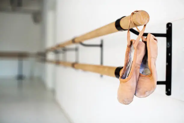 Ballet shoes hanging on wooden barre. Pair of ballet slippers hanging from handrail. It is in dance studio.