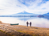 アジア カップル旅行者で 30 代 40 代にスタンドの手を握るし、河口湖の側の地面に朝時間富士山を背景にボートで写真を撮る