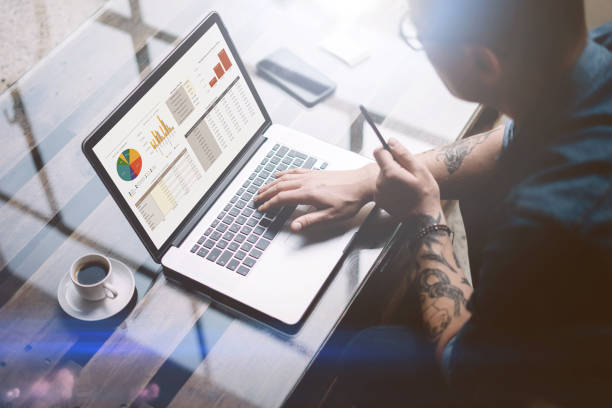 istock Adult tattooed businessman working on mobile computer at sunny office.Man typing on notebook keyboard.Graphs and diagramm on laptop screen.Horizontal,blurred background. 815170080