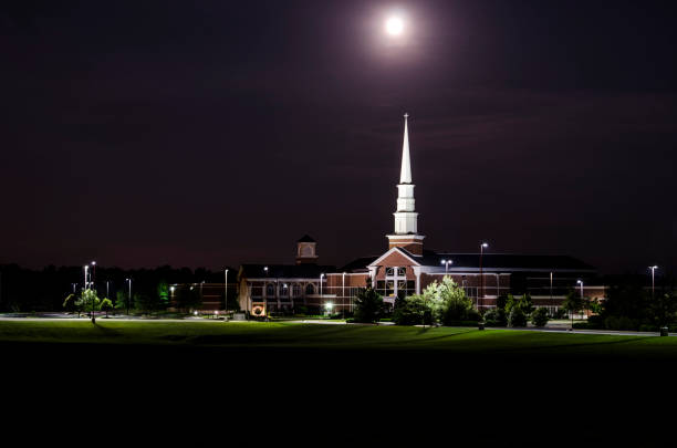 A cloud-filtered moon illuminates a Christian church steeple and campus.