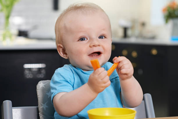 niño feliz sentado en la mesa comiendo zanahorias frescas - baby carrot fotografías e imágenes de stock