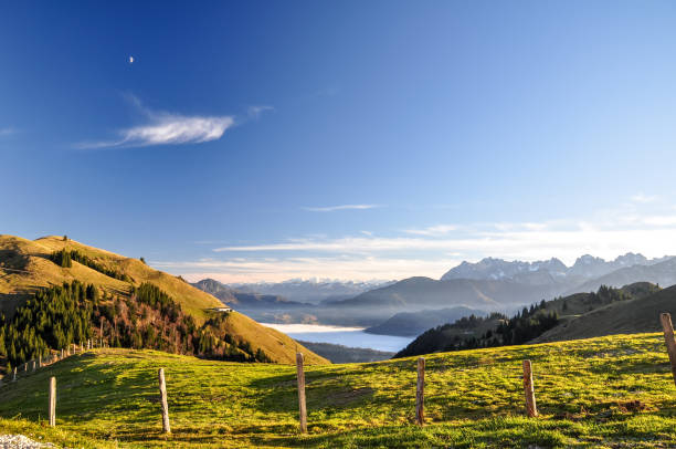 Beautiful evening view near Wandberg mountain in the Chiemgau Alps mountain range in Austria. Tranquil scene with a fence, a fresh lawn and mountains in the background and fog in the lowland. stock photo