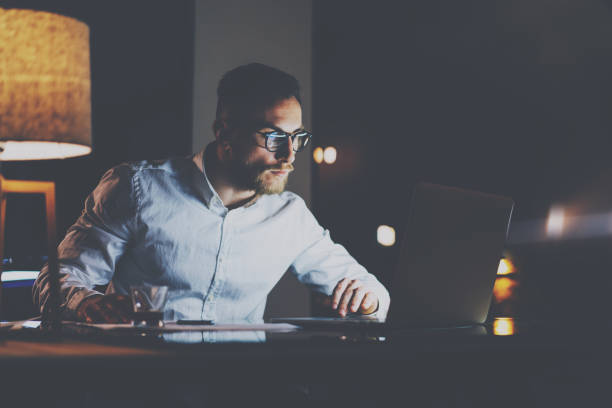 istock Bearded young businessman in eyeglasses working at office at night.Man using laptop.Horizontal, bokeh effect, reflections. 815202602