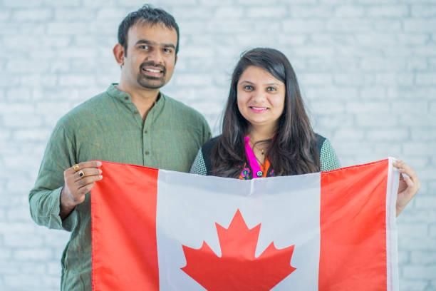 Big Canadian Flag An Indian husband and wife are indoors in a new home. They are wearing Indian-style clothing. They are posing while holding a large Canadian flag in front of them. citizenship photos stock pictures, royalty-free photos & images