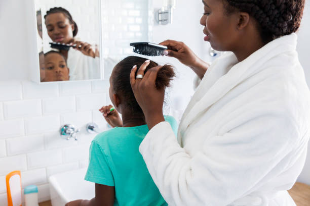 Mother brushing her daughters hair. Young african female in the bathroom with her daughter brushing her hair. brushing hair stock pictures, royalty-free photos & images