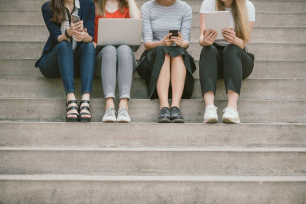 istock Low section of young female friends holding technologies while sitting on steps 815381936