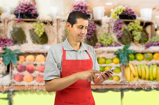 shopman with apron uses a smart phone at the fruits store