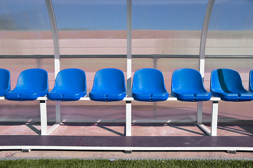 sport bench with red plastic seats in the stadium players outdoors with blue paint under transparent plastic roof as banking players