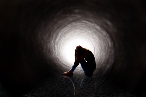 A depressed woman sitting in a dark tunnel with her reflection in the water.