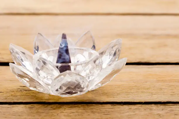 Photo of Burning incense cone in crystal lotus holder with wafting smoke on wooden background