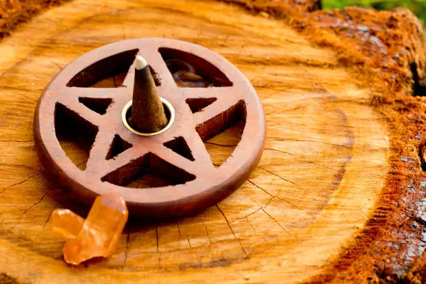 Photo of Burning incense cone  in wooden pentacle incense holder on natural cut tree log with crystal