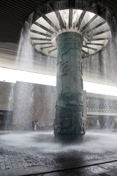 Impressive fountain at the entrance with tourists and Mexican families in the background. Major Mexico City tourist attraction, the National Museum of Anthropology, designed by Pedro Ramirez Vasquez, houses antiquity artifacts representing all major regional Mexican cultural and ethnic groups. World class, impressive displays and architecture.