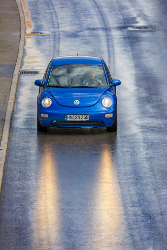 Frankfurt, Germany - July 12, 2017 : Blue VW Beetle driving on a wet highway near the city of Frankfurt in Germany on a summer day with headlights on