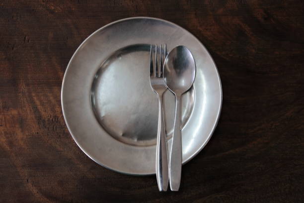 istock Round clean stainless plate with fork spoon on a dark wood table. top view for copy space. 815509552
