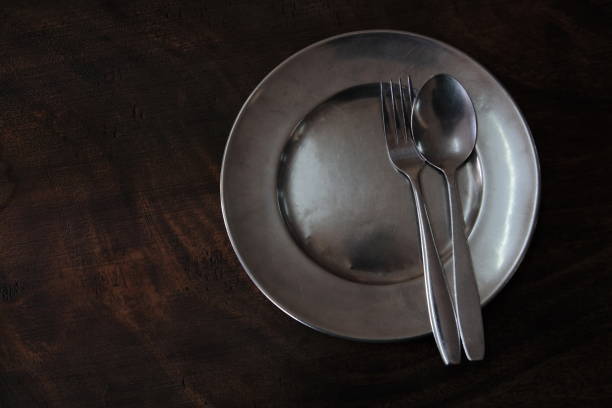 istock Round clean stainless plate with fork spoon on a dark wood table. top view for copy space. 815509564