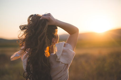 Rear view of young hipster woman watching sunset on a wheat field