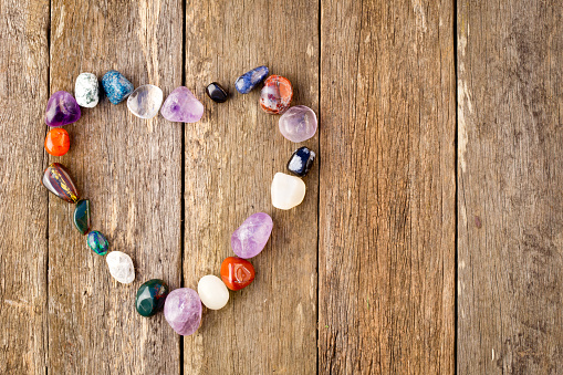 Tumbled healing crystals in heart shape on wooden background