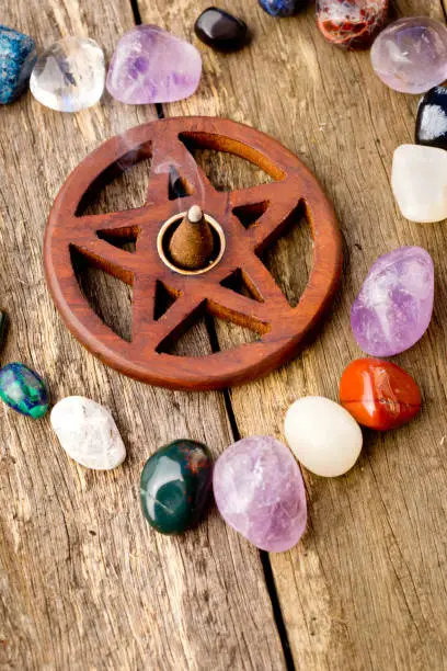 Photo of Incense burning in wooden pentagram burner with crystals in heart shape on wooden background