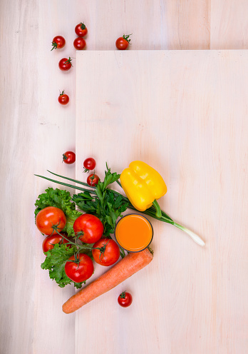 Tomatoes on a light brown wooden background. A variety of tasty and healthful vegetables: carrot, tomatoes, salad pepper, onions on a table.  A fresh orange juice near vegetables. Food ingredients.
