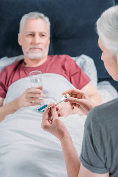 istock woman looking at thermometer while taking care of sick husband 815582150