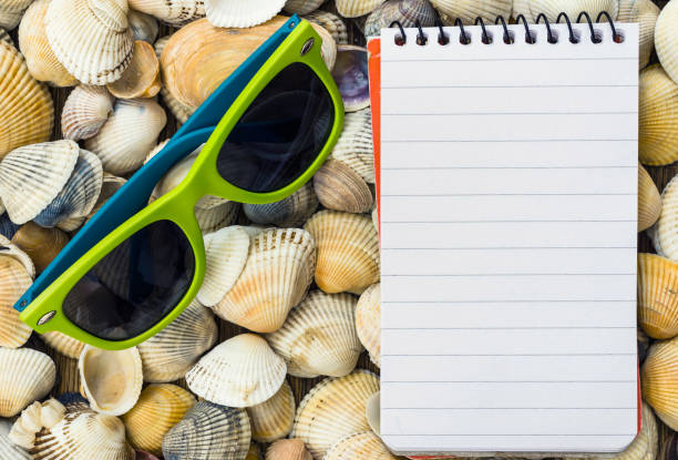 Blank spiral notebook and seashells with sunglasses. Beach background with copy space. Image for background.