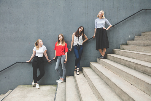 Full length portrait of confident young women standing against wall