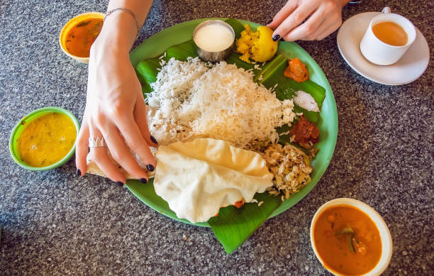 Hands of woman on table with traditional South Indian food thali with rice and spicy vegetables on palm leaf. Hands of woman on table with traditional South Indian food thali with rice and spicy vegetables on palm leaf. Asian kitchen still-life. soup lentil healthy eating dishware stock pictures, royalty-free photos & images