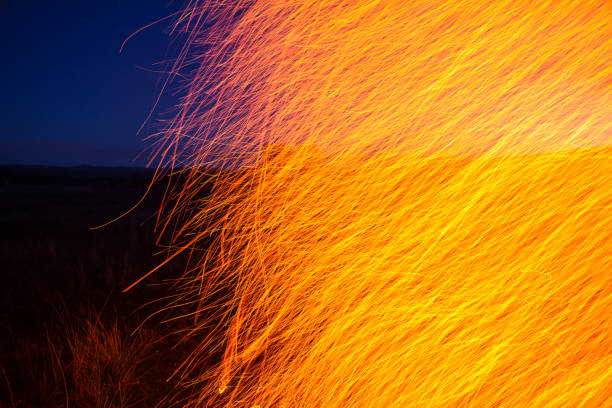 A slow shutter speed makes this fire appear distorted with the sparks stretching out into lines. This is shot against a twilight sky.