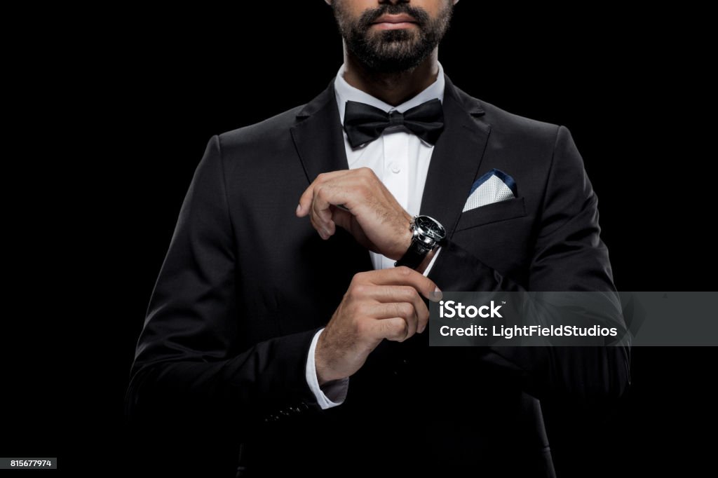 cropped view of businessman in bow tie and tuxedo with watch, isolated on black Tuxedo Stock Photo