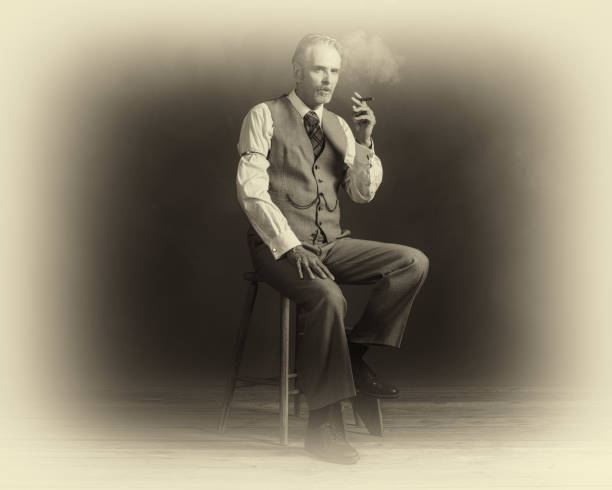 foto antica di sigari che fumano uomo vintage degli anni '20 che indossa un abito seduto su sgabello di legno. - 20s adult camera caucasian foto e immagini stock