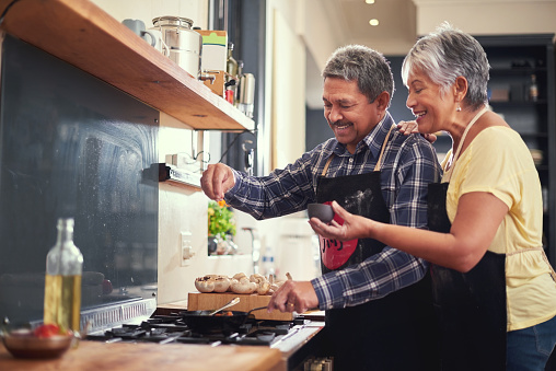 Shot of a happy mature couple adding salt to a dish while cooking together at home