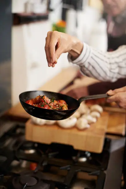 Cropped shot of a unrecognizable person's hand adding salt to a pan of tomatoes in the kitchen
