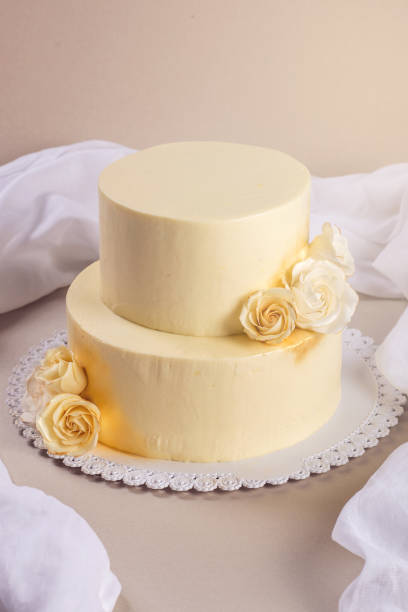 istock Beige 2 tiered wedding cake decorated with mastic roses stands on fabric background 815701898