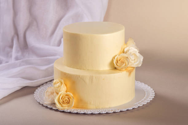 istock Beige 2 tiered wedding cake decorated with mastic roses stands on fabric background 815701926