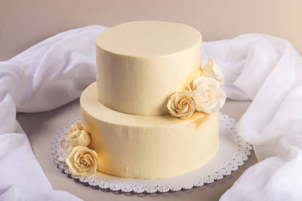 istock Beige 2 tiered wedding cake decorated with mastic roses stands on fabric background 815701944